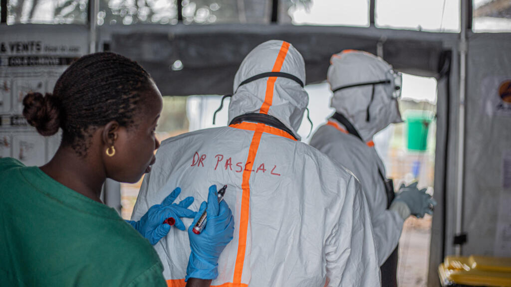 Un agent d'hygiène écrit le nom d'un médecin au dos de sa combinaison de protection avant d'entrer dans un centre de traitement Ebola situé à Rwampara pour soigner des patients atteints de la maladie, à Bunia (Ituri), dans l'est de la République démocratique du Congo, en juillet 2026.